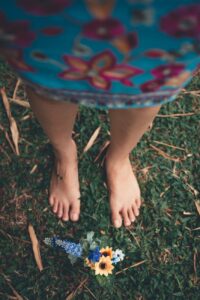 selective focus photography of woman's bare feet in the grass in front of flowers